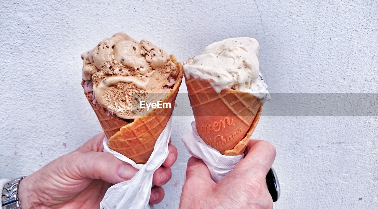 Close-up of hands holding ice cream cones against wall