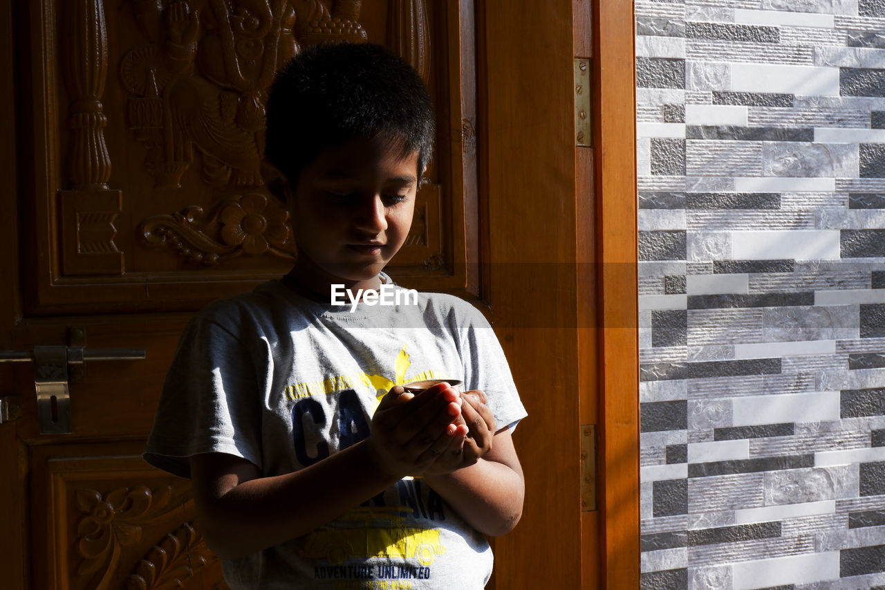 Cute boy holding cup standing by door