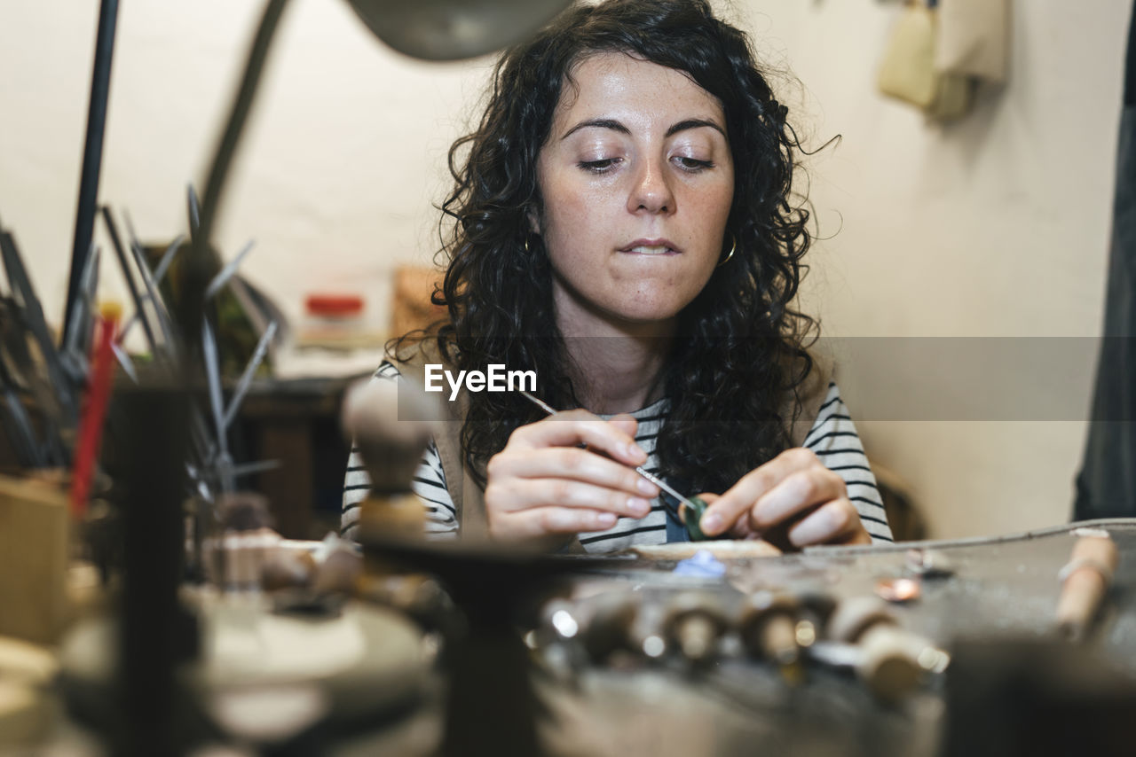 Midsection of female artisan making ring while sitting at table in workshop