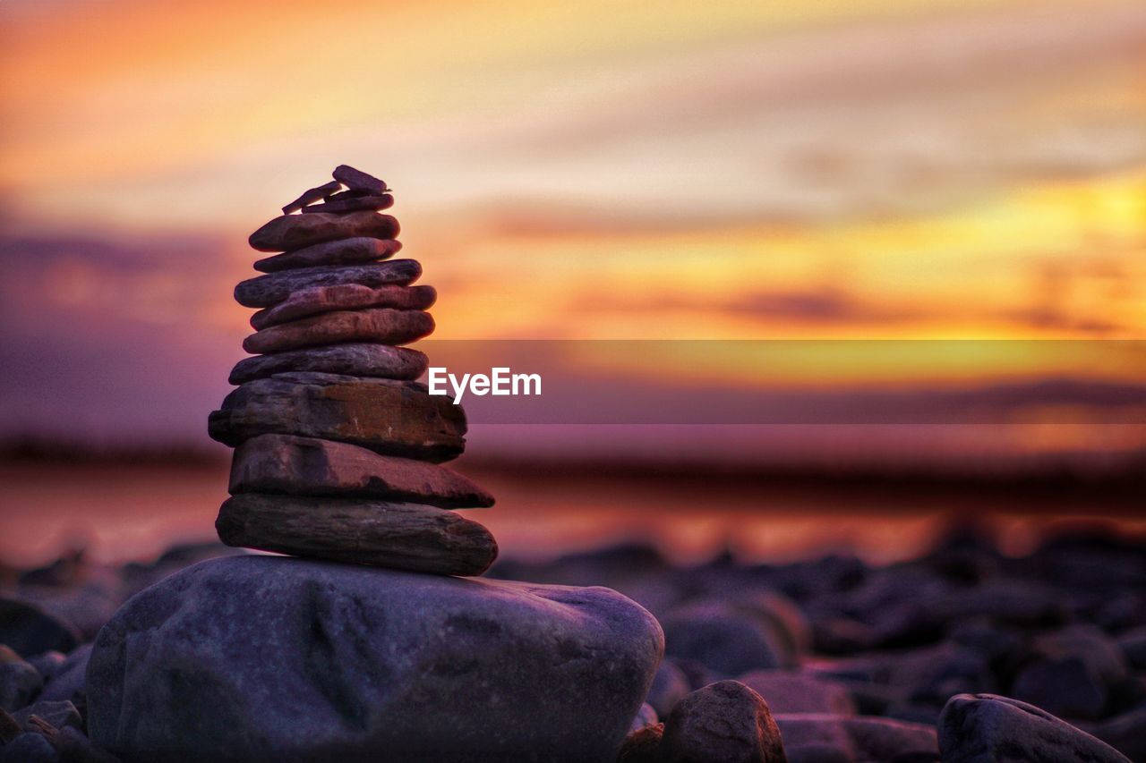Stack of stones at beach against sea and sky during sunset