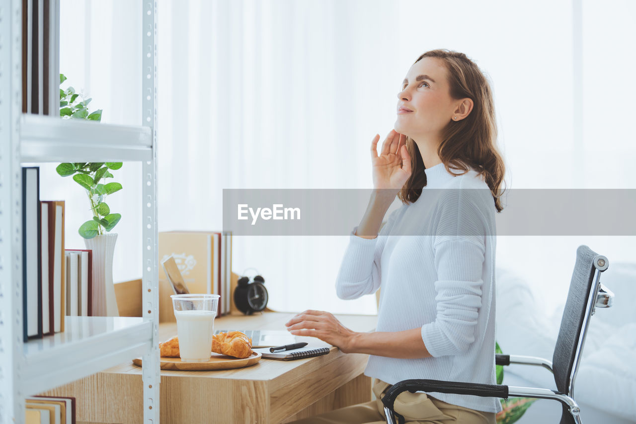 Thoughtful woman looking away while sitting with breakfast on table at home