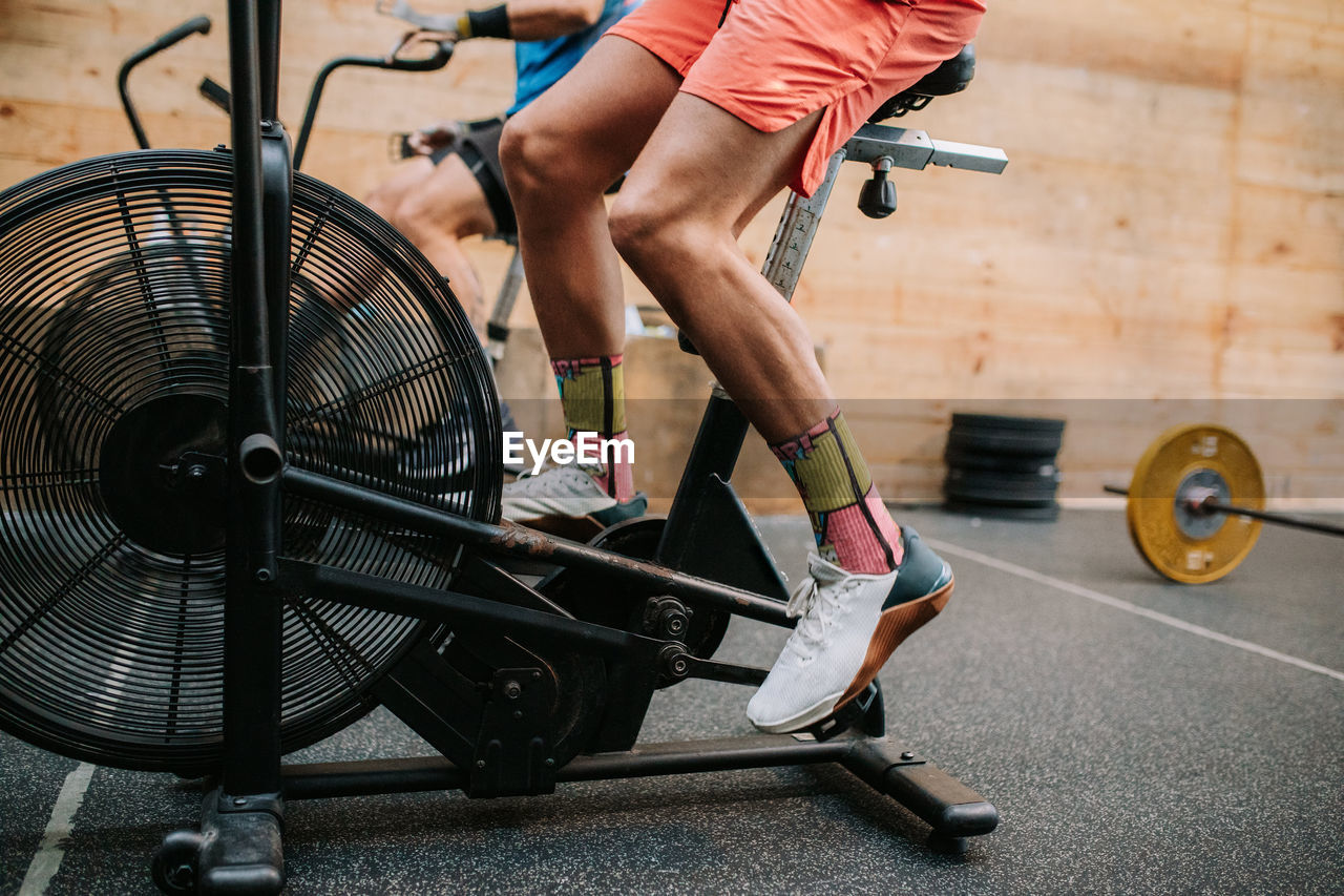 Cropped unrecognizable active male athletes doing exercises on air cycling machines during intense workout in gym