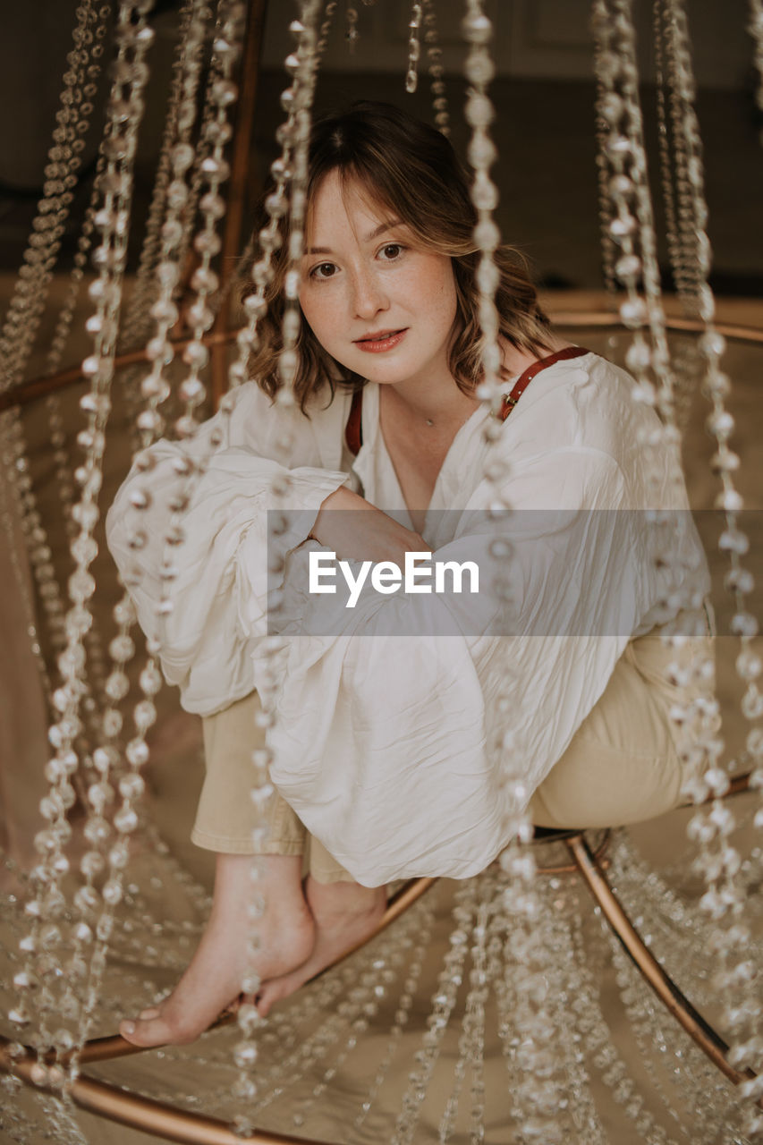 Young female in victorian shirt sitting in giant crystal chandelier and smile