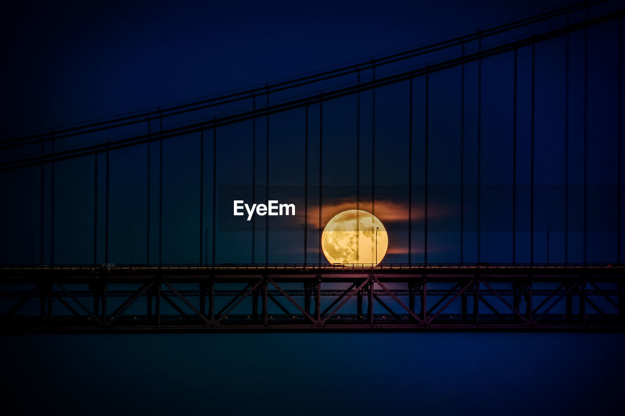 Silhouette suspension bridge against moon at night