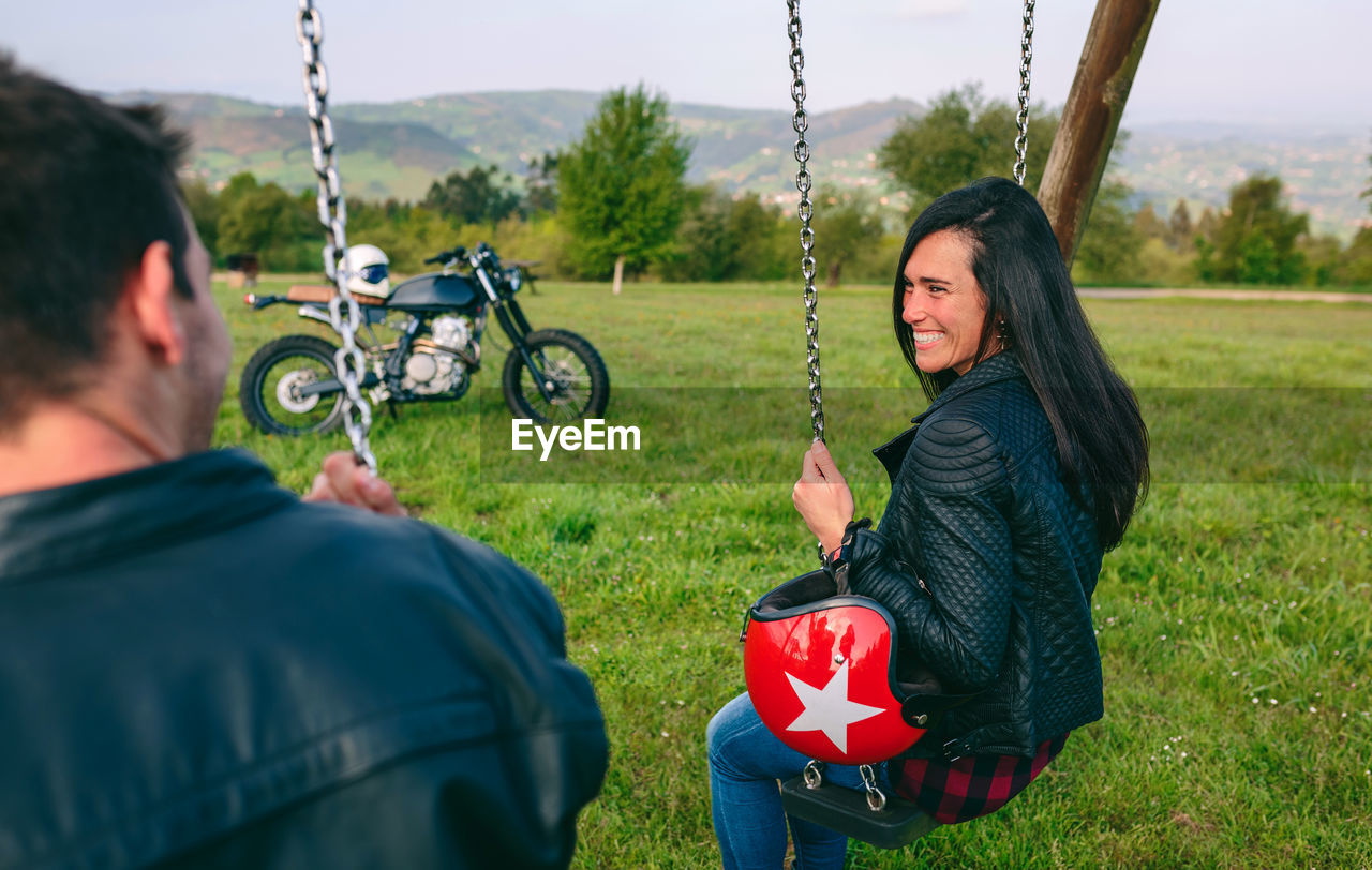 Happy young woman looking at her boyfriend sitting on a swing in a recreational area
