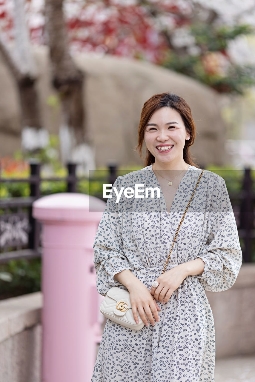 PORTRAIT OF SMILING WOMAN STANDING OUTDOORS