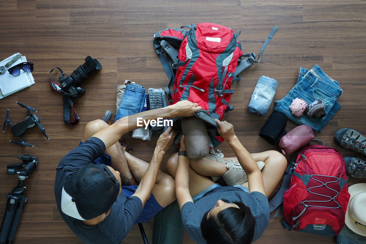 High angle view of people packing backpack on hardwood floor