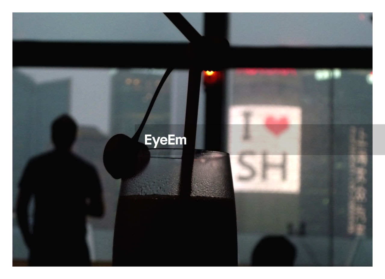 Close-up of silhouette drink by man against illuminated buildings at dusk