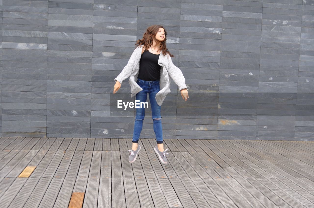 Front view of teenage girl jumping against gray wall