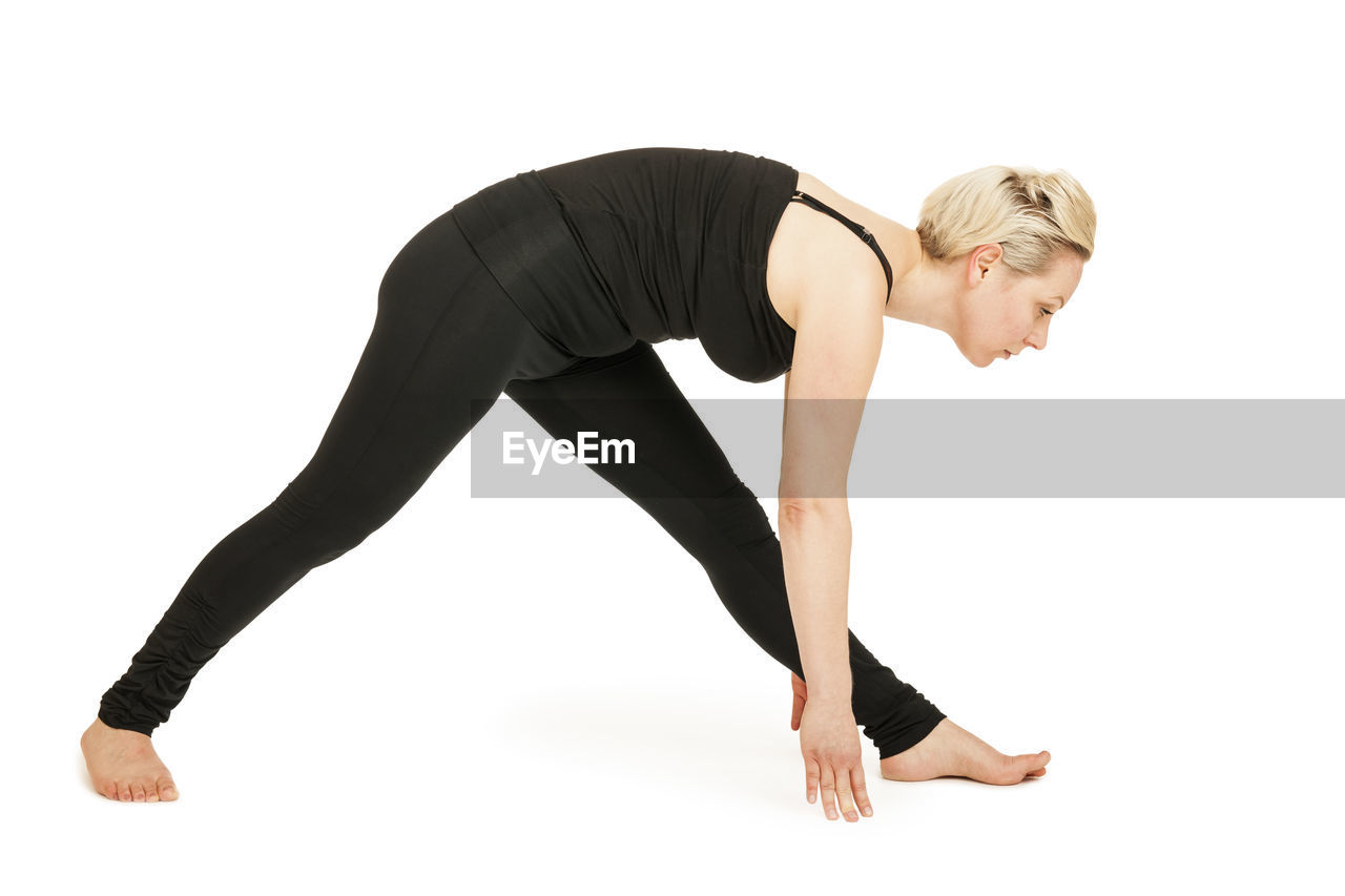 Full length side view of mid adult woman practicing yoga against white background