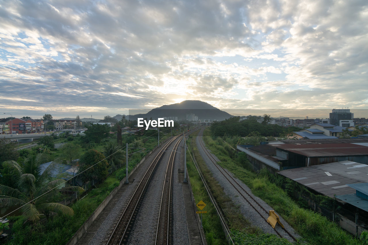 sky, architecture, cloud, transportation, rail transportation, city, railroad track, track, built structure, nature, building exterior, travel, sunset, landscape, environment, mode of transportation, building, transport, high angle view, travel destinations, horizon, no people, plant, cityscape, outdoors, train, public transportation, residential area, mountain, scenics - nature, railway, road, beauty in nature, street, residential district, sunlight, land, city life, urban skyline, business finance and industry