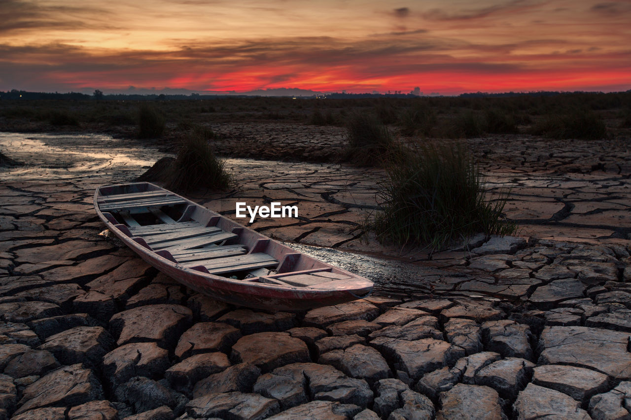 Boat on drought land against sky during sunset