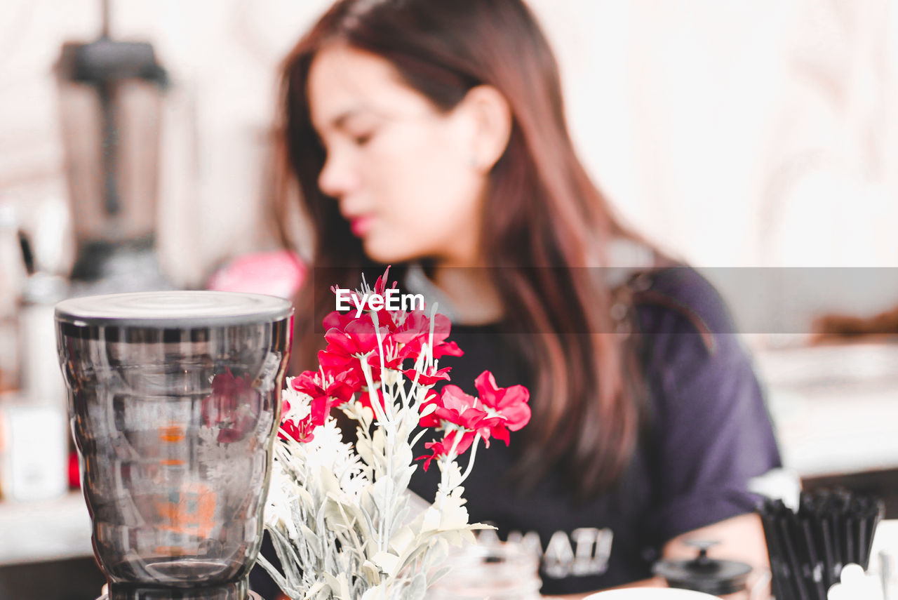 CLOSE-UP OF WOMAN WITH RED FLOWER ON TABLE AT HOME