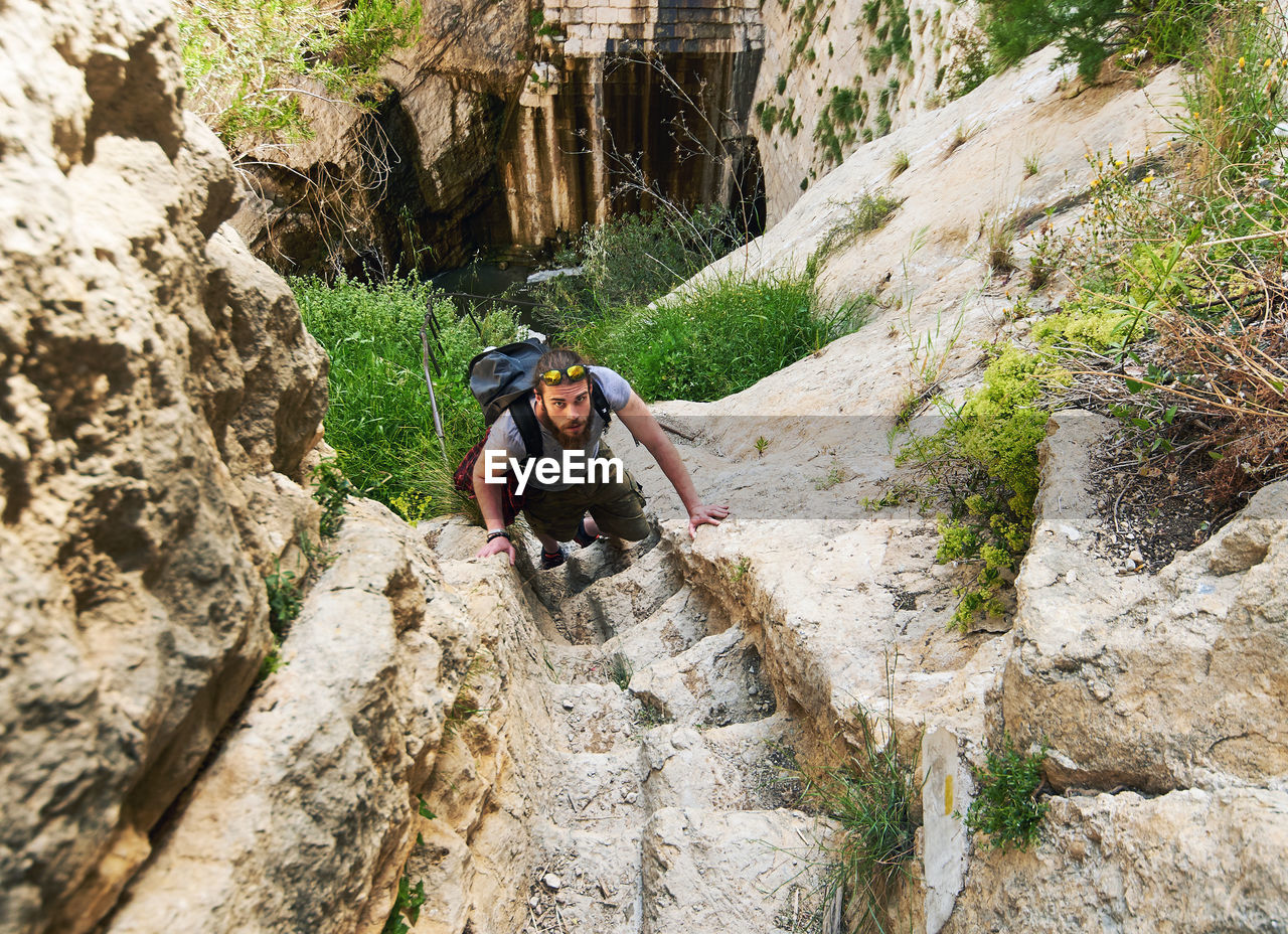 Portrait of man moving up on rock by mountain