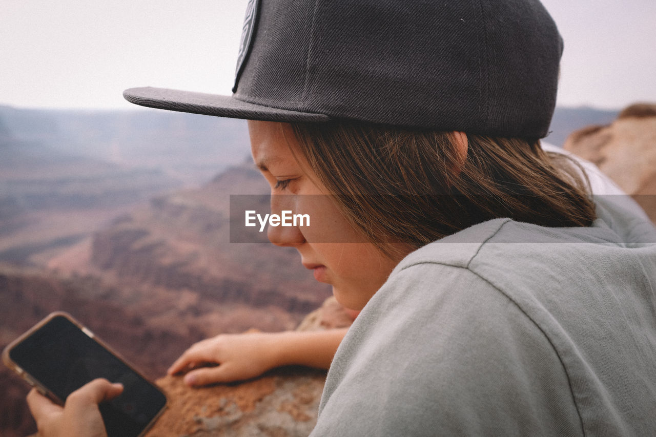 Boy checking his phone over a canyon overlook