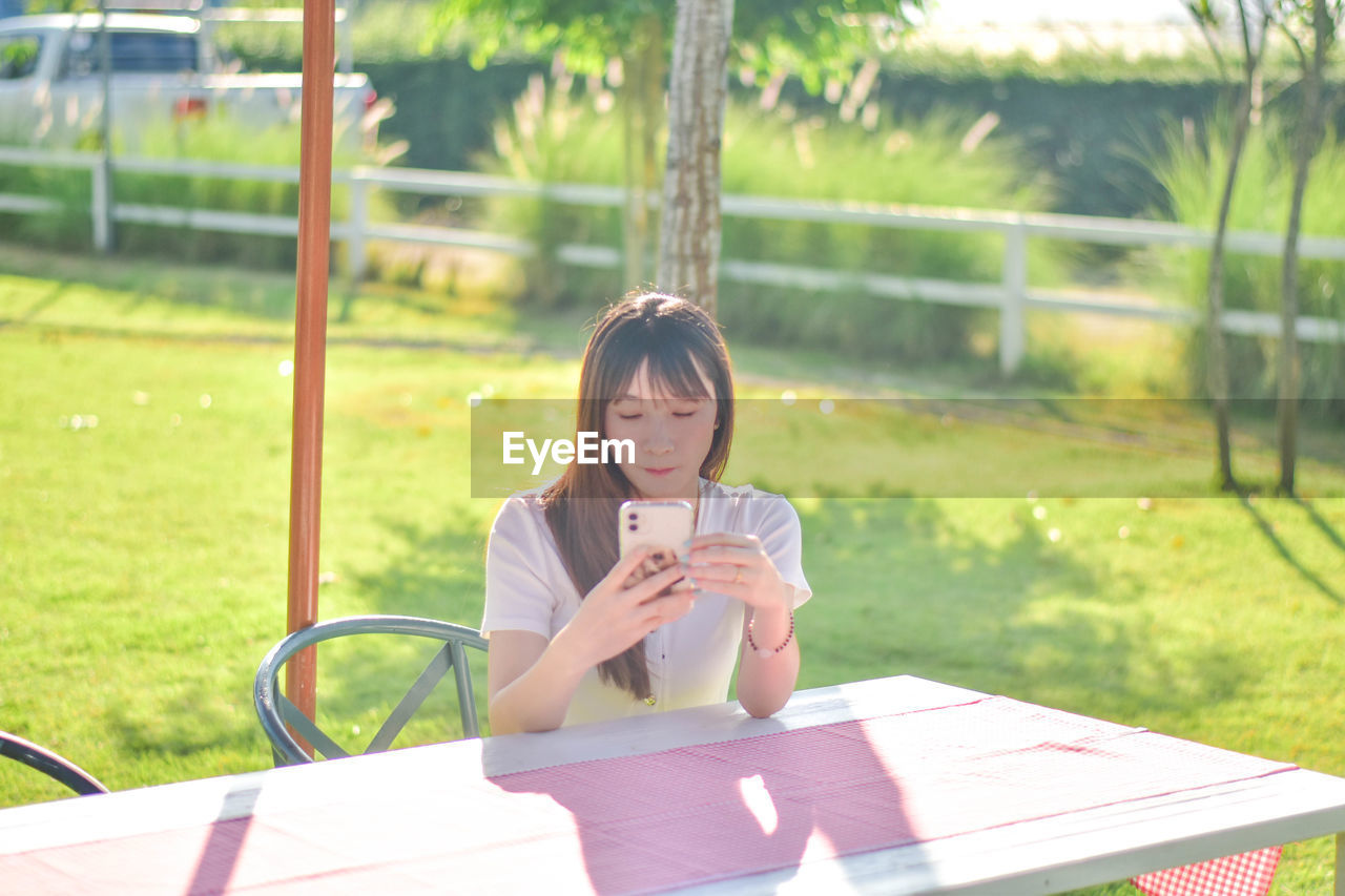 young woman using mobile phone while sitting on field