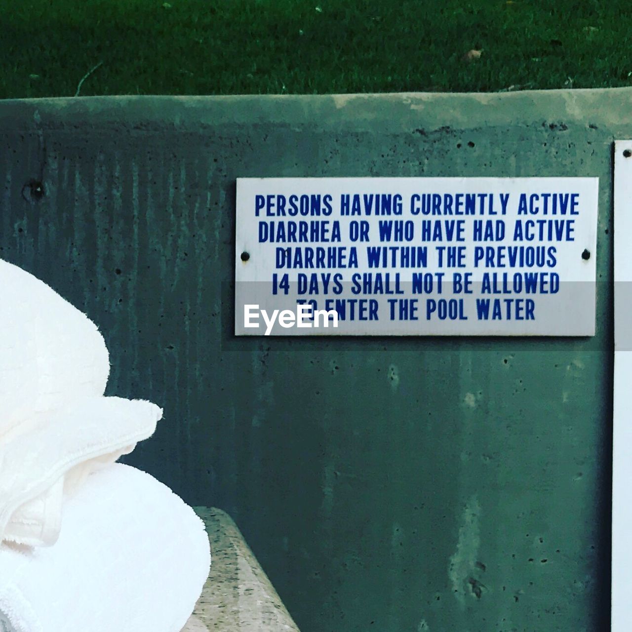 Sign board with text on retaining wall at poolside