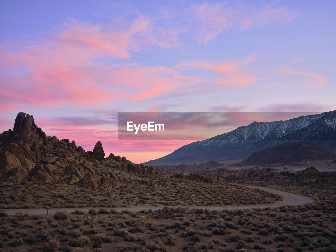 Cotton candy clouds, a dirt road winds through rock formations.