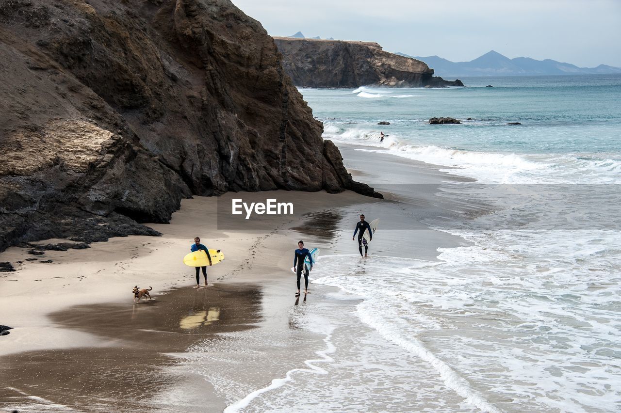 PEOPLE WALKING ON BEACH AGAINST MOUNTAIN