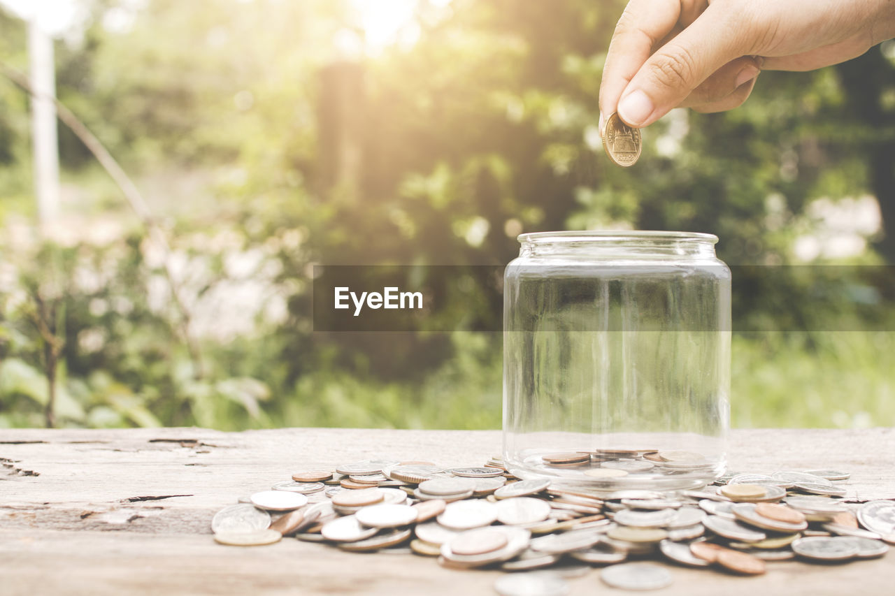 Close-up of hand inserting coin in glass jar on table