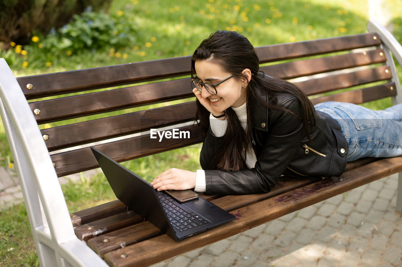 Young woman using laptop while sitting on bench