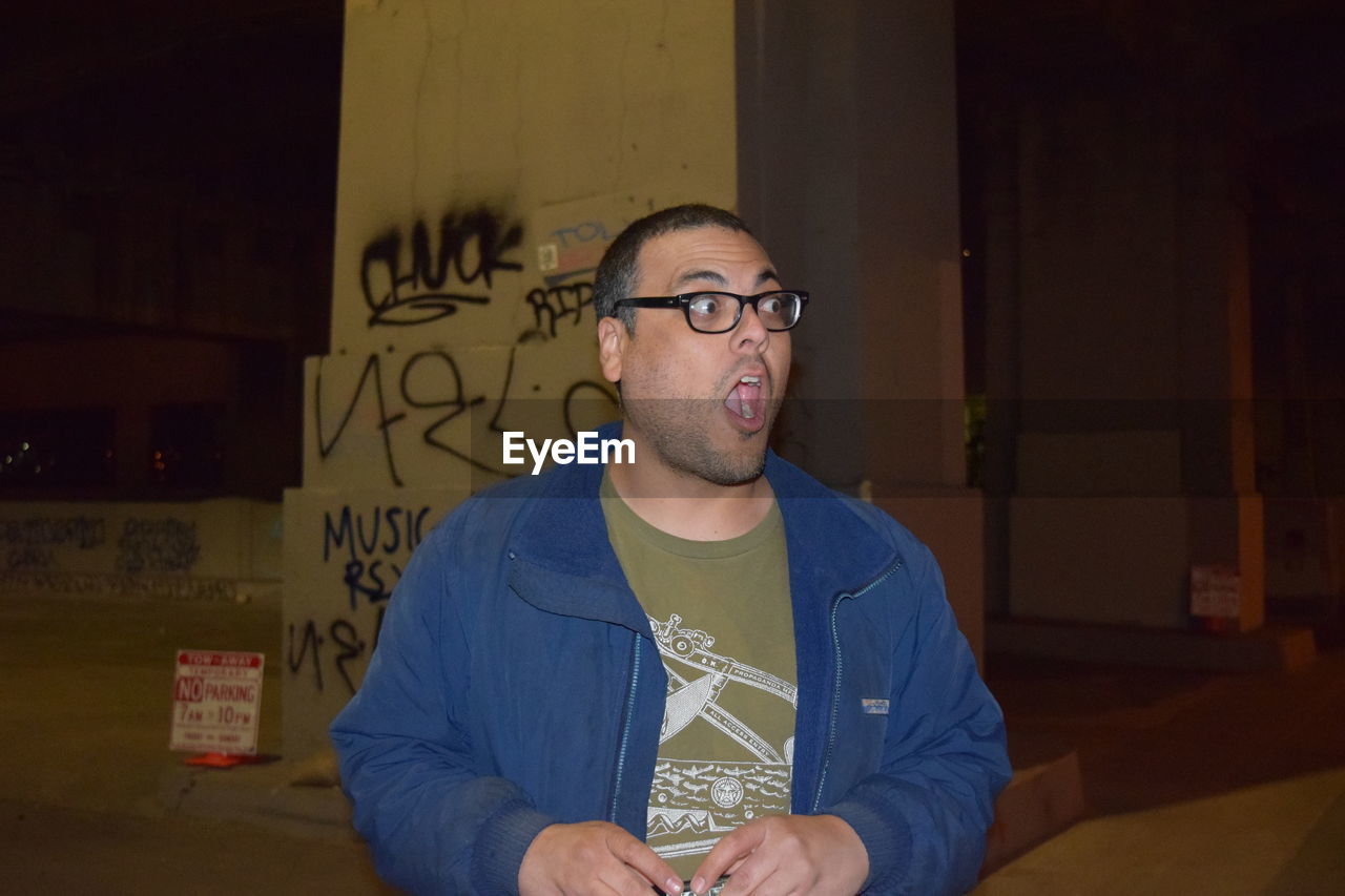 Surprised man with mouth open looking away by bridge at night