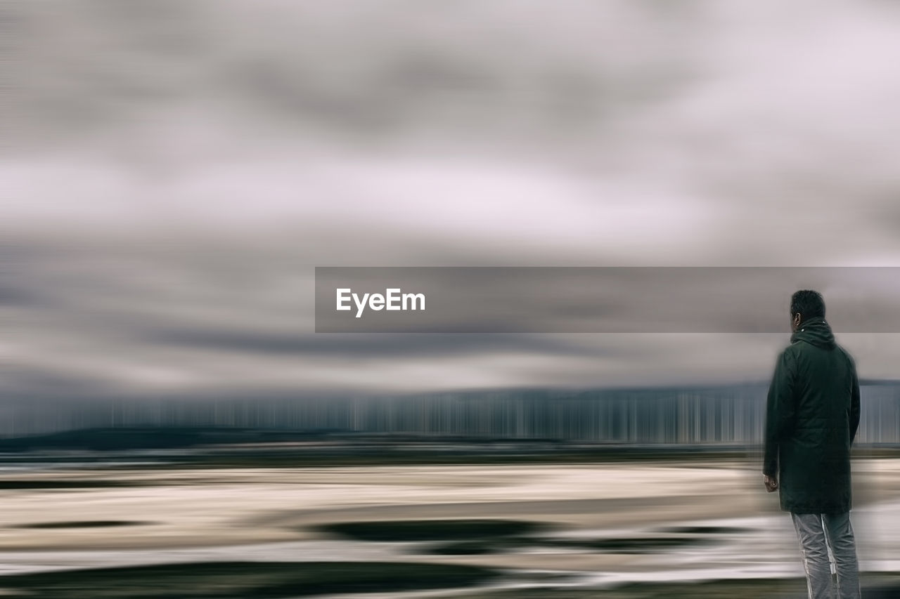 Rear view of man standing on road against cloudy sky