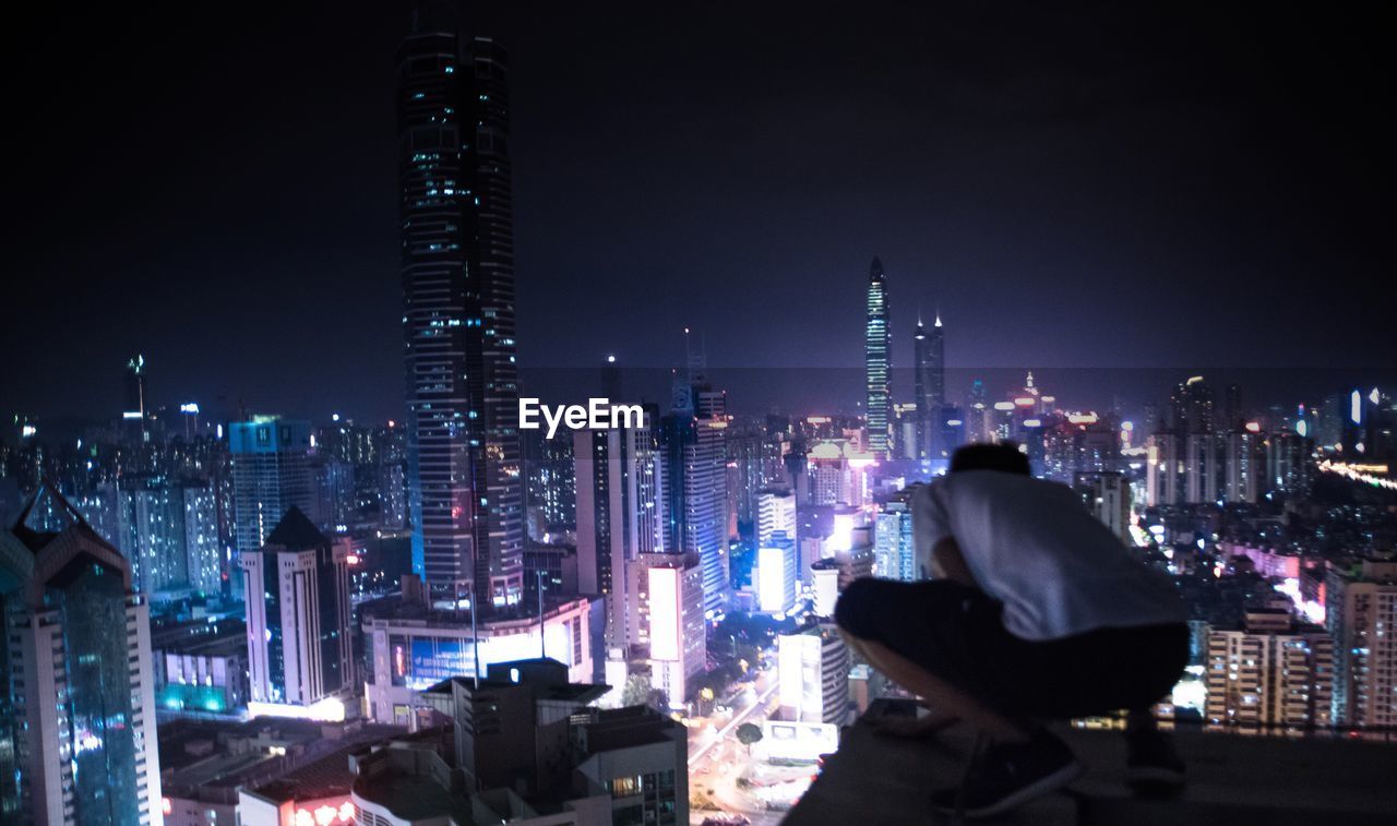 Rear view of man with illuminated cityscape in background