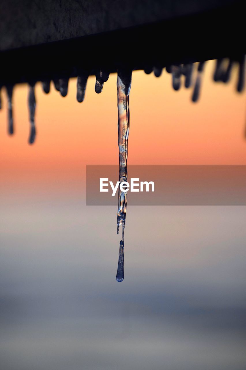 CLOSE-UP OF ICICLES AGAINST SKY AT SUNSET