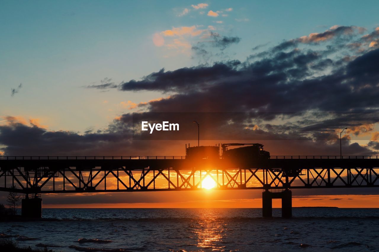 Silhouette bridge over sea against sky during sunset