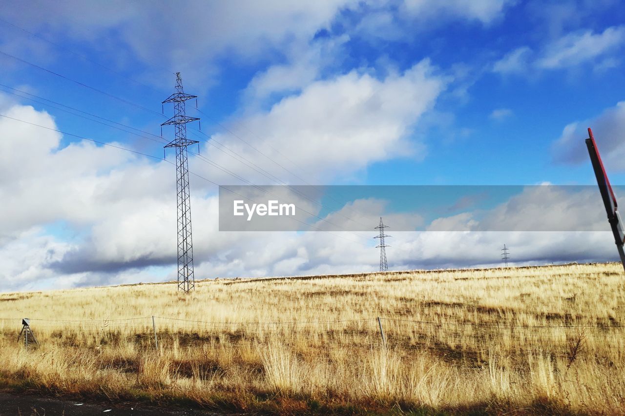 ELECTRICITY PYLONS ON FIELD AGAINST CLOUDY SKY
