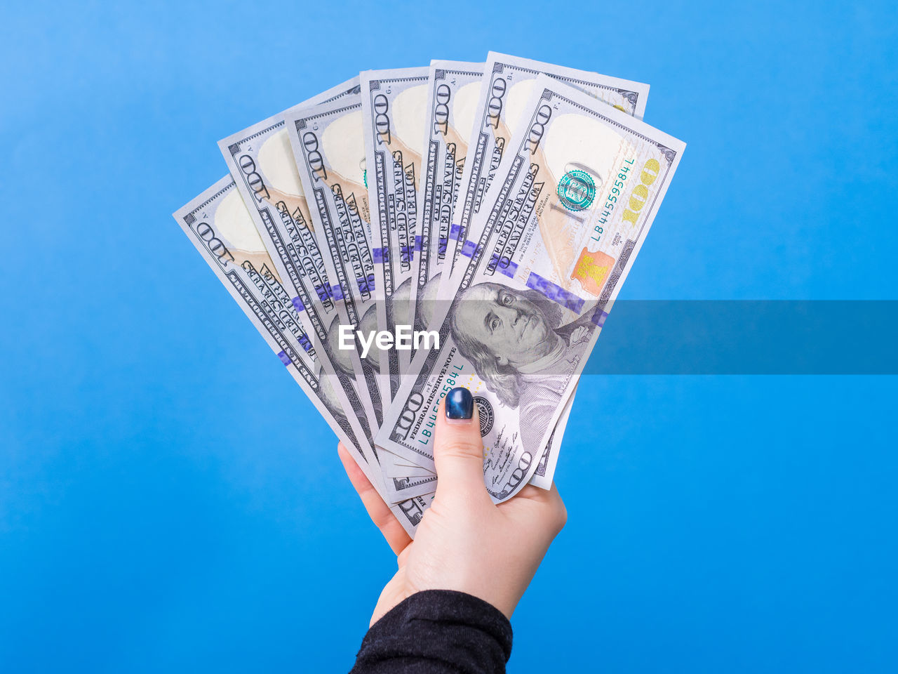 Cropped hand of woman holding paper currency against blue background
