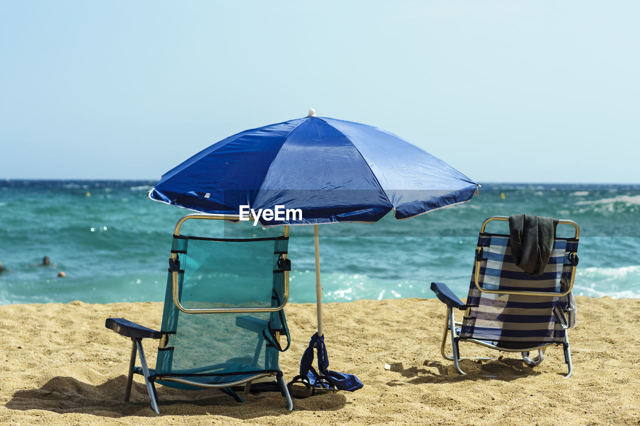 Deck chairs at beach against clear sky