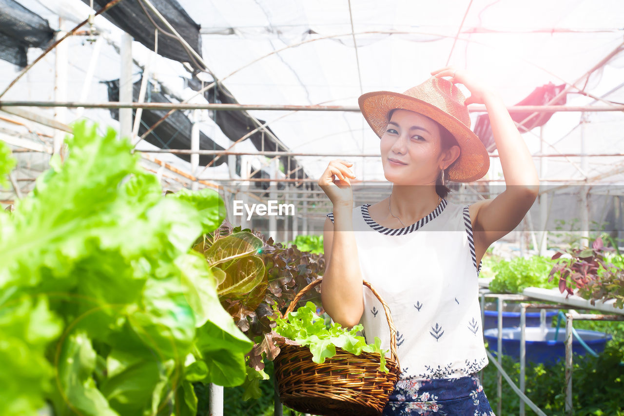 Portrait of woman holding vegetables while standing in greenhouse