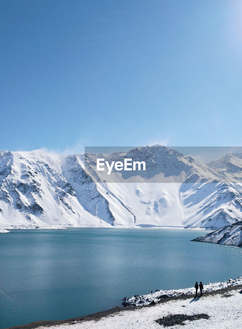 Scenic view of snowcapped mountains by lake against clear blue sky
