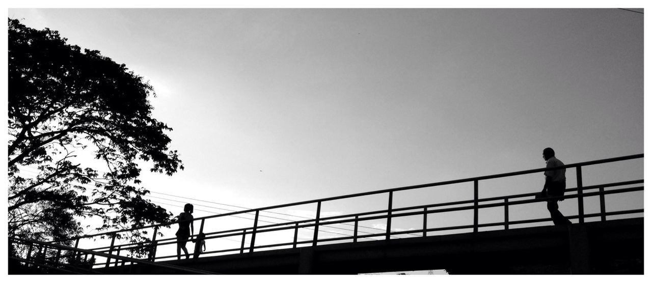 Low angle view of silhouette people walking on walkway bridge against clear sky at dusk