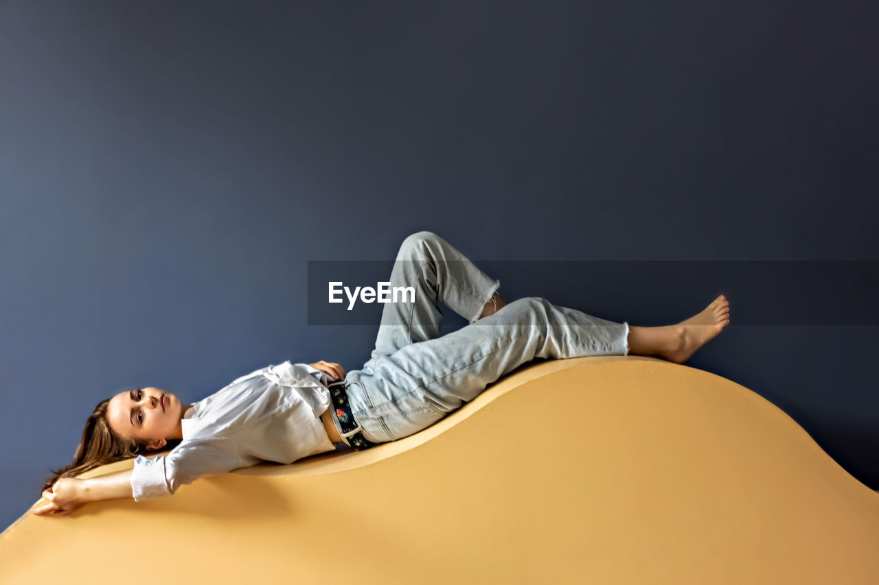 Portrait of a young woman lying on a geometric sand-colored couch.abstract.