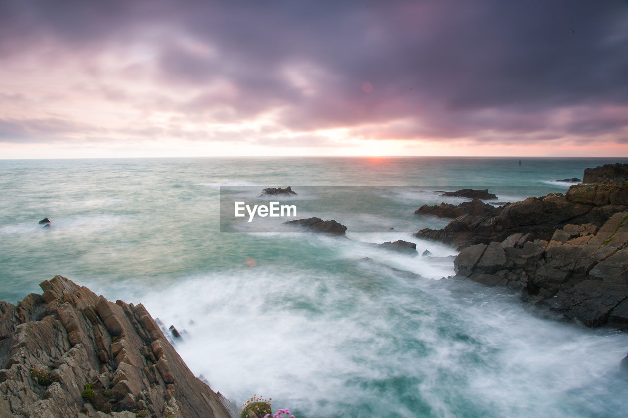 Scenic view of sea against cloudy sky during sunset