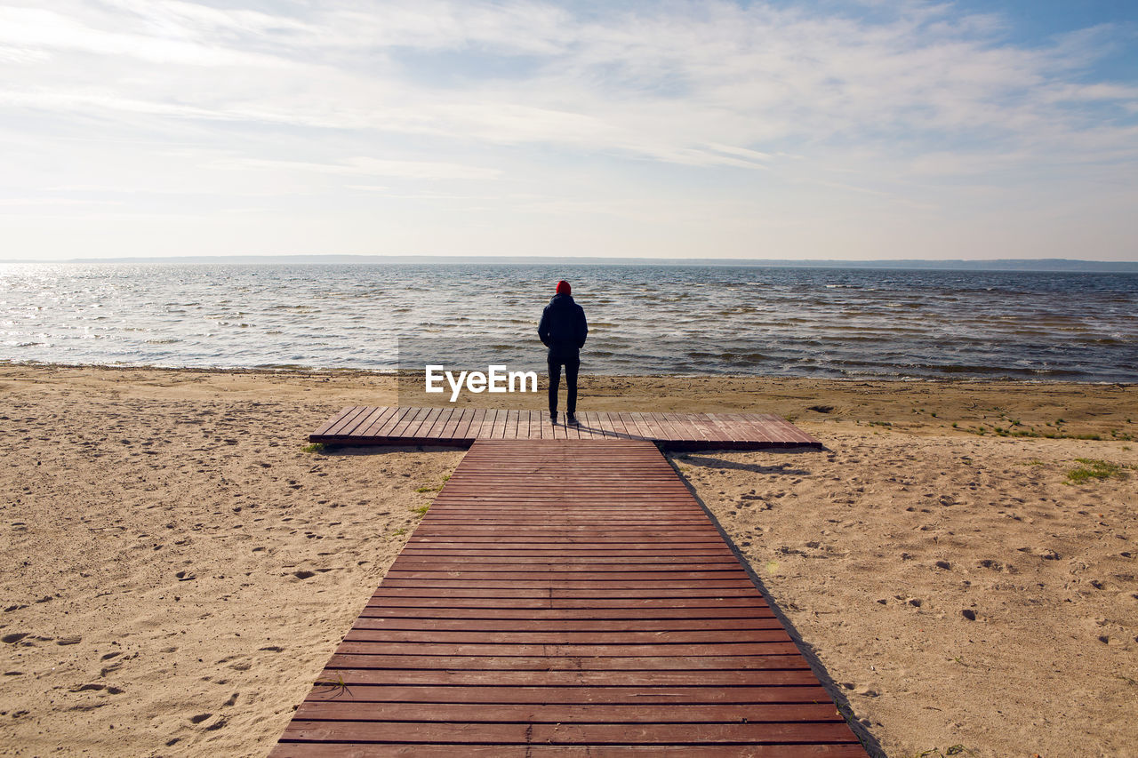 A man in a black jacket stands on a wooden platform by the lake