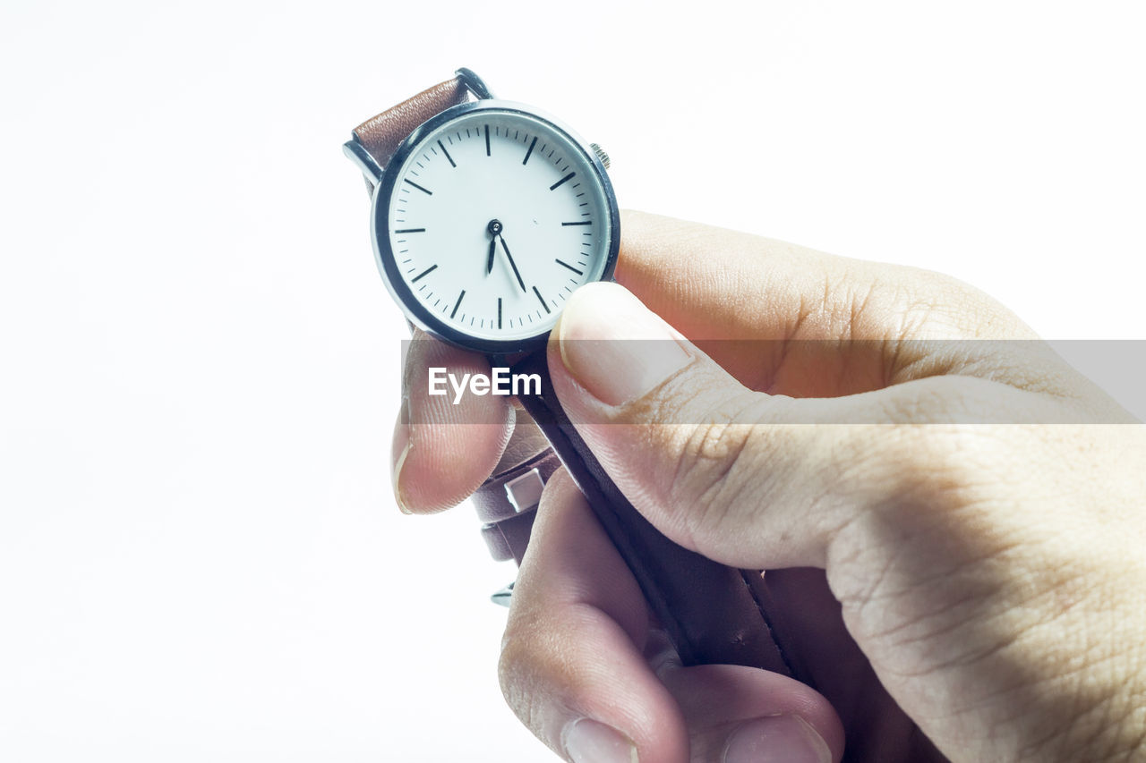 HUMAN HAND HOLDING CLOCK AGAINST WHITE BACKGROUND