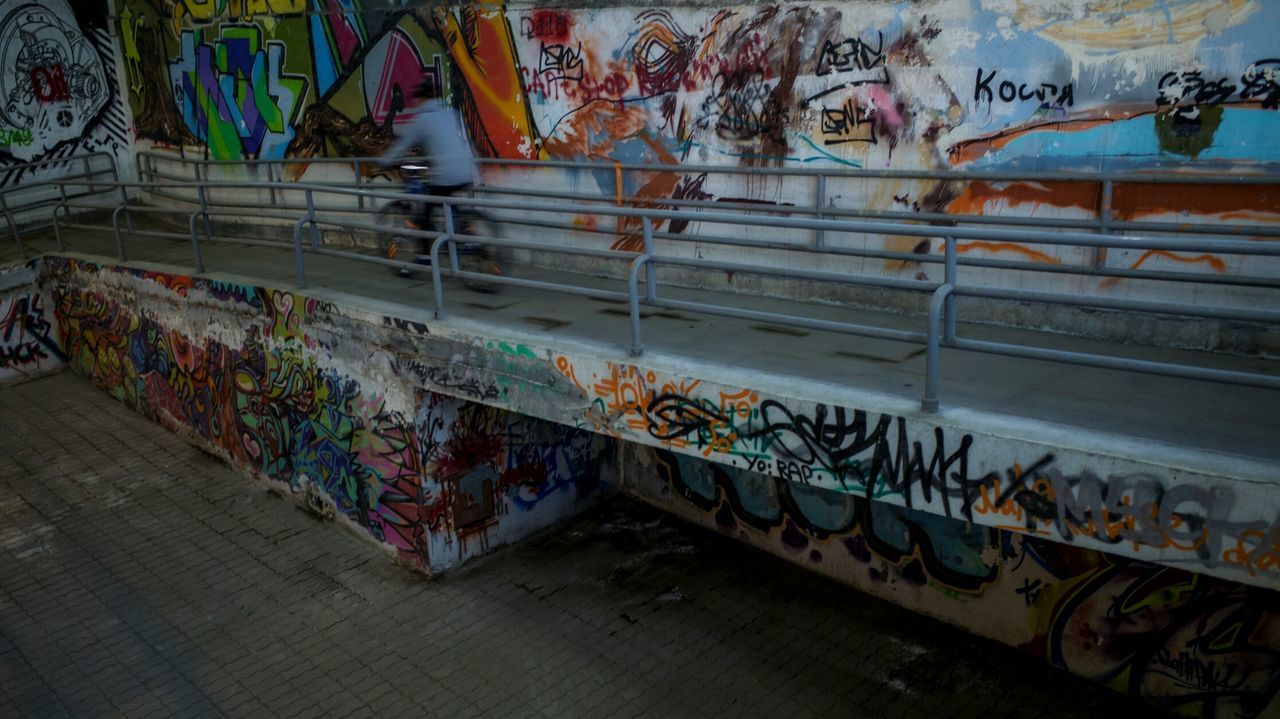 Man cycling on elevated walkway by graffiti wall