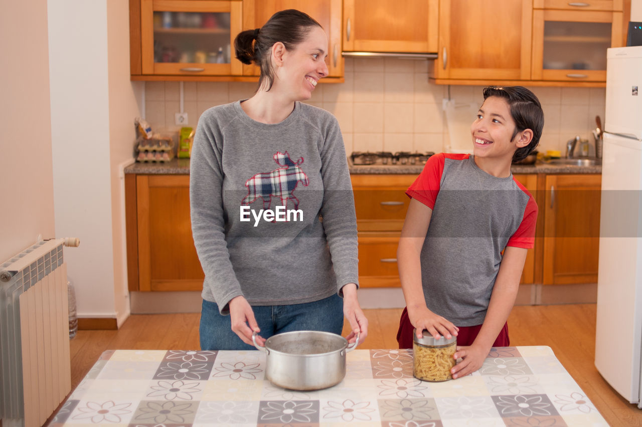 Smiling mother teaching son while preparing food at home