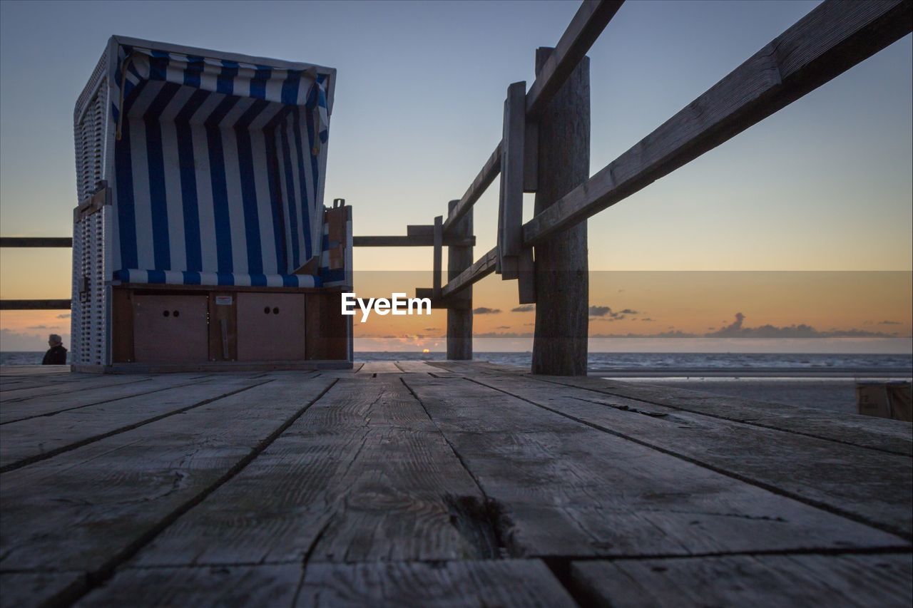 Hooded beach chair on wooden pier by sea against sky during sunset