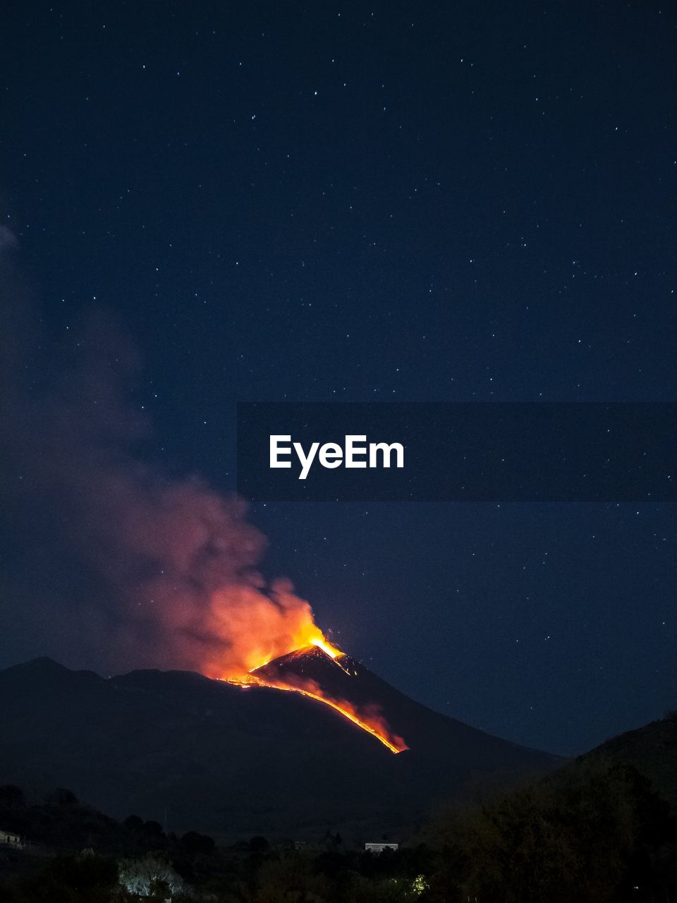 Panoramic view of the etna volcano illuminated by lava and the night sky.