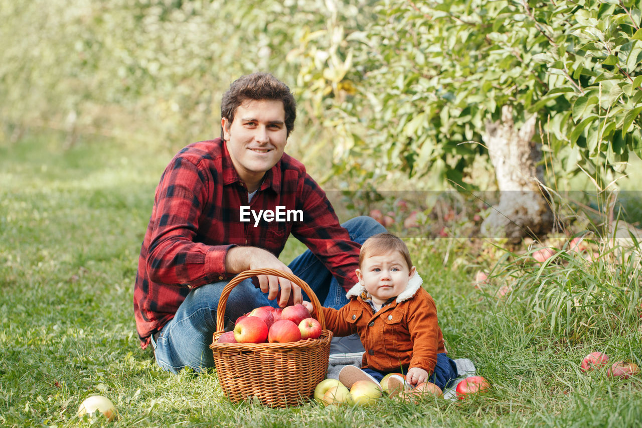 Portrait of happy father and son sitting while fruits in basket at park