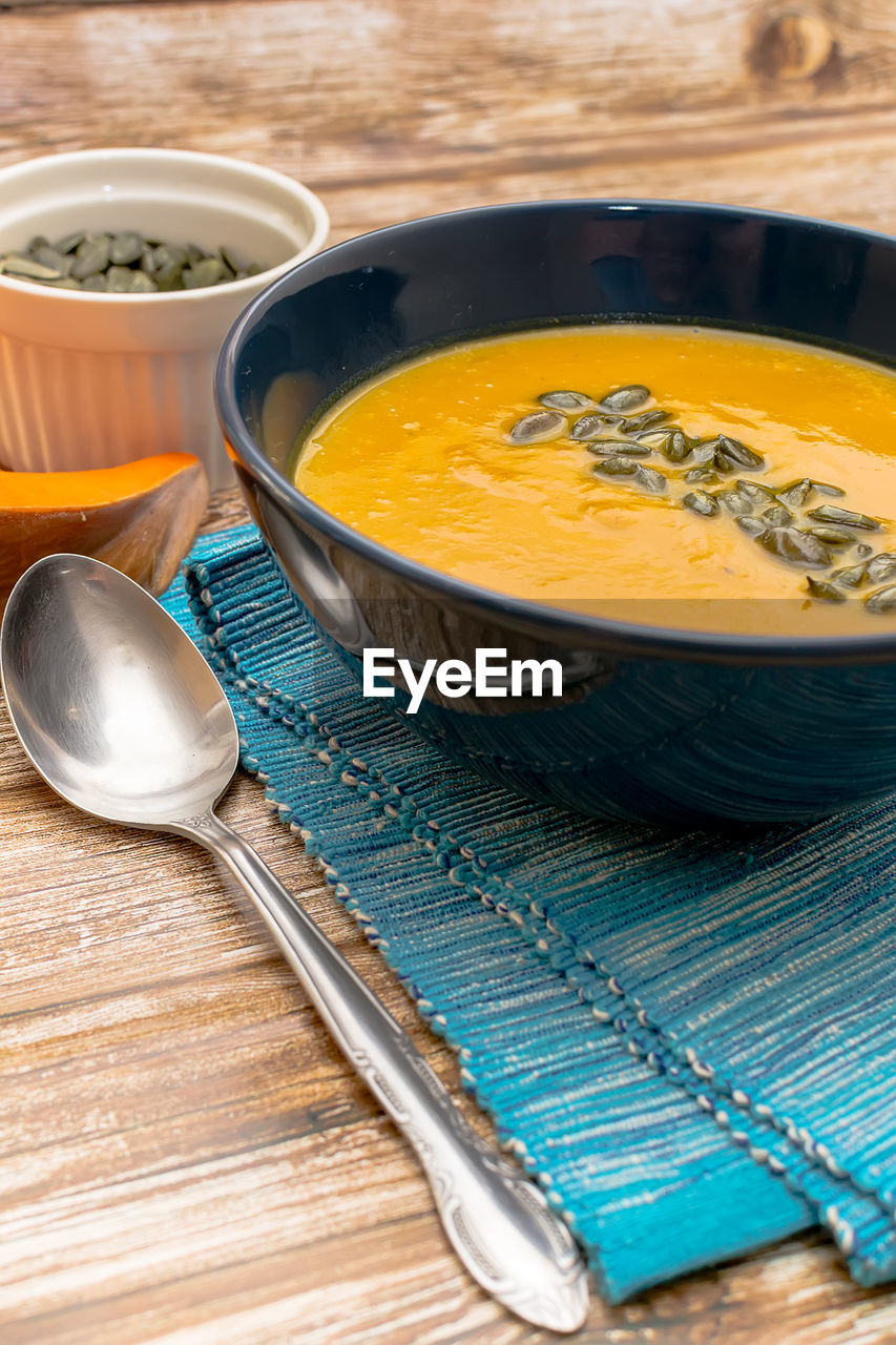 Cream pumpkin soup garnished with pumpkin seeds on a wooden table