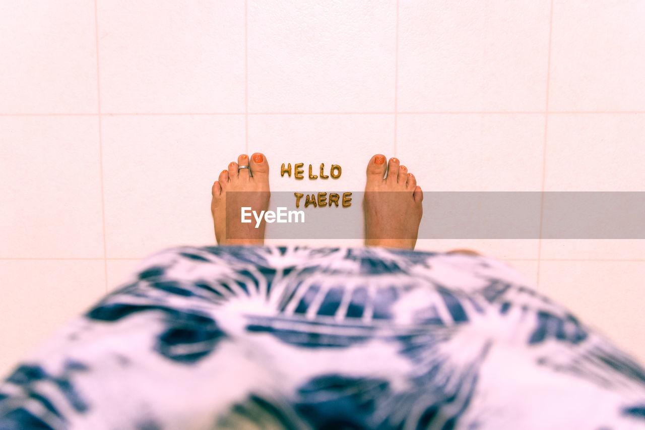Low section of woman with hello there text on tiled floor
