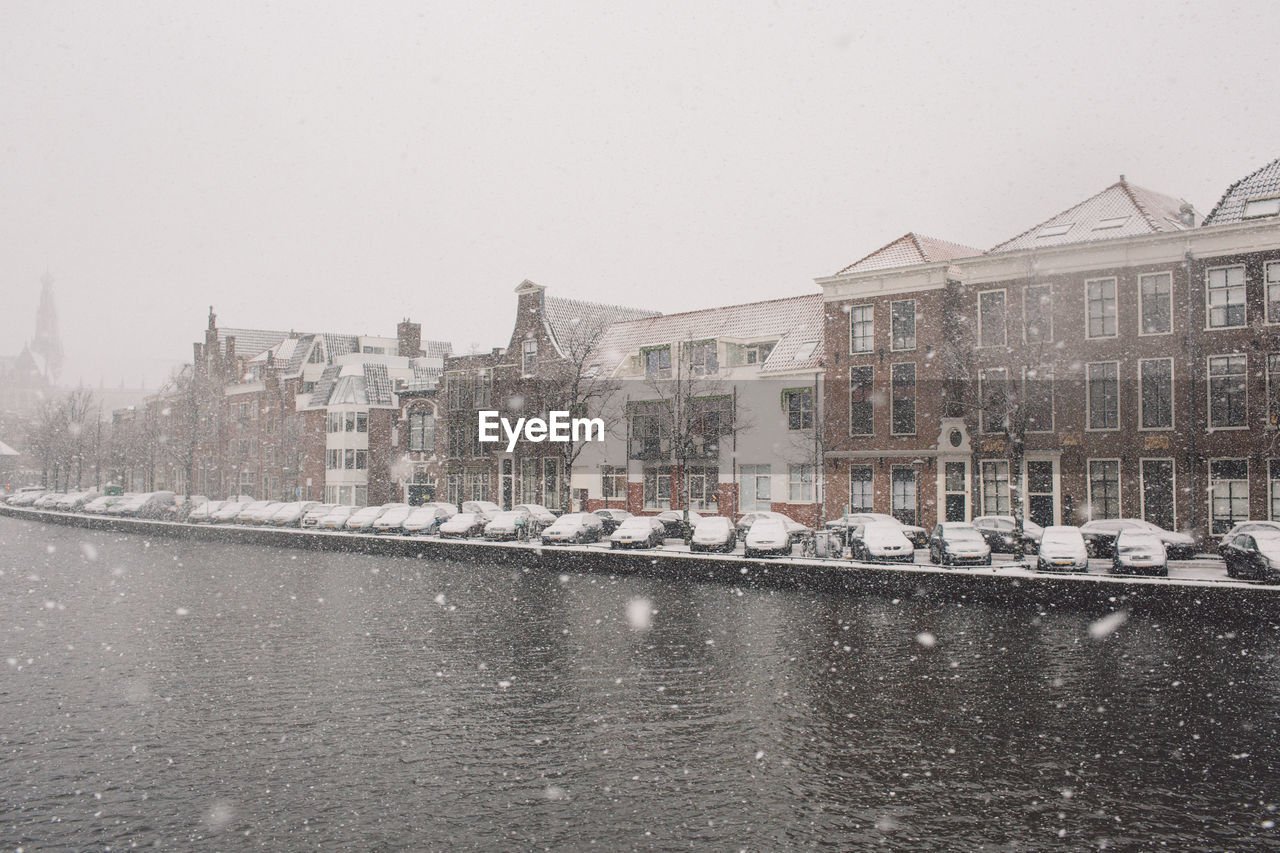 River by buildings against sky during snowfall