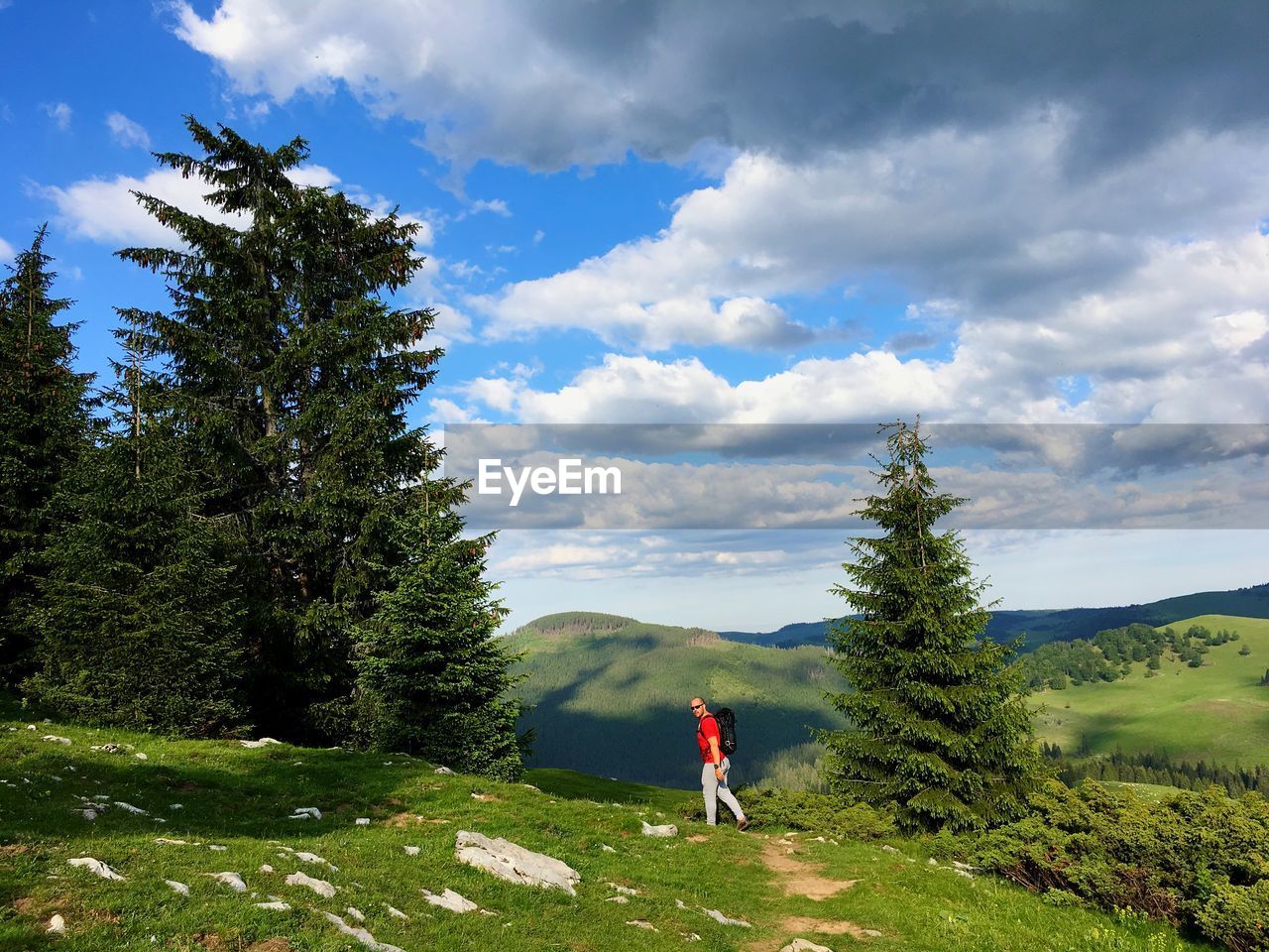 Side view of young man walking on green landscape against cloudy sky