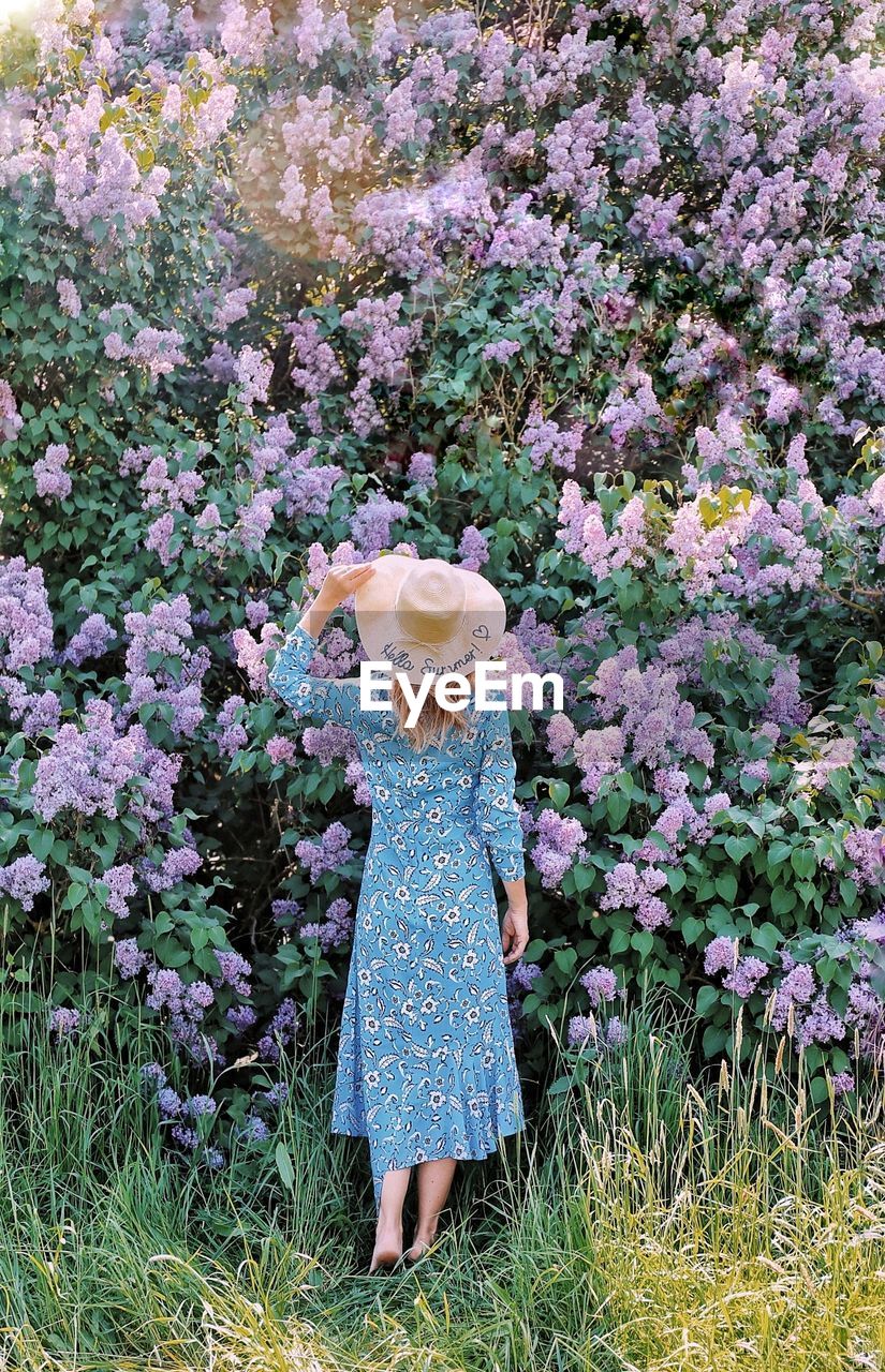 WOMAN STANDING BY FLOWERING PLANTS